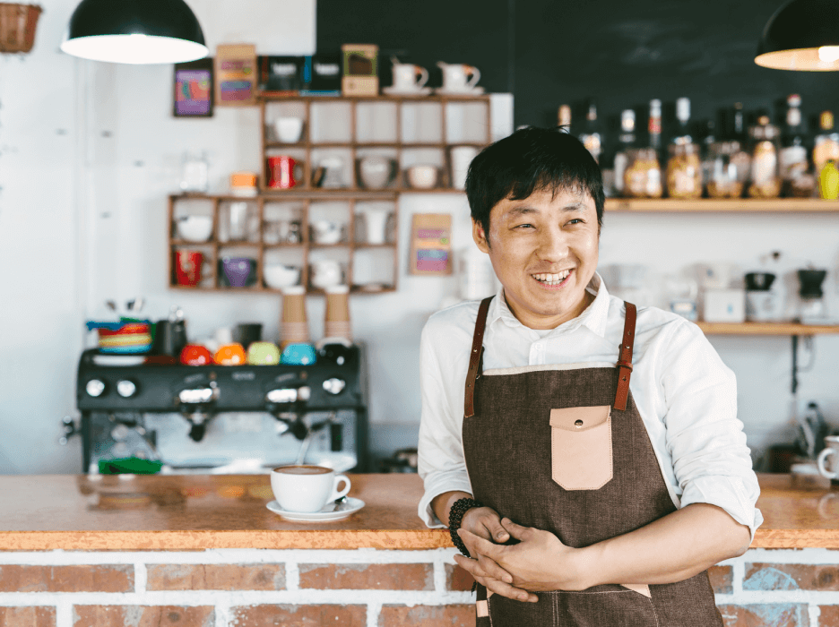 A smiling small business owner with an apron at a coffee shop. 