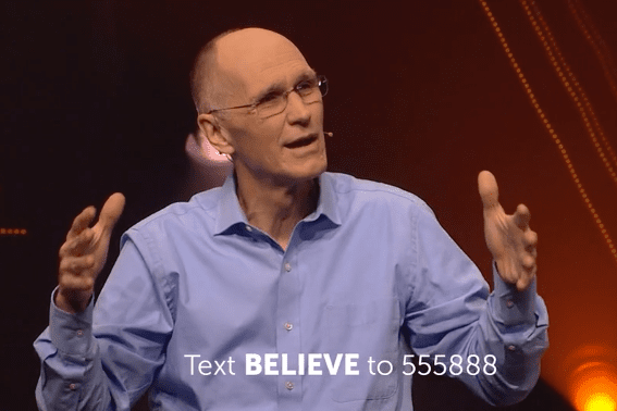 Preacher with arms outspread, overset text reading "Text BELIEVE to 555888"