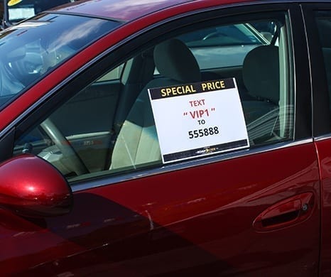 Poster with sign, Text VIP1 to 555888, in driver window of red car