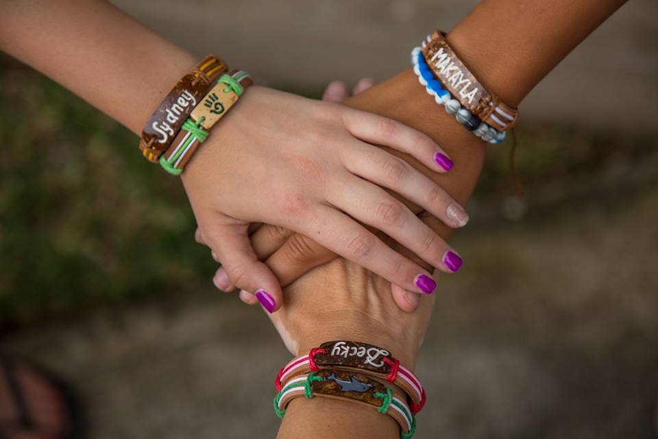 Three hands stacked on top of each other, with arms wearing Yuda Bands with names on them