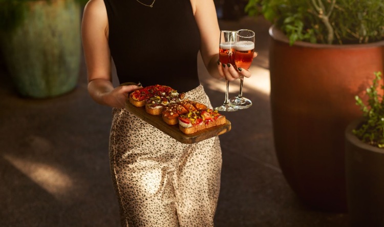 Woman bringing a platter of bruschetta and wine to a table in a restaurant