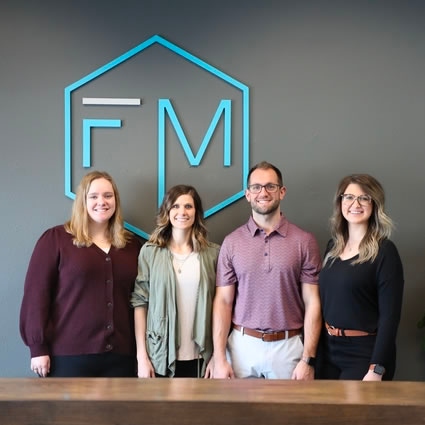 FM Chiropractic team of four people stand in their office with a company logo on the wall behind them