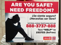 A sign on a bathroom mirror titled “Are you safe? Need freedom?” featuring a hotline number and text keyword for human trafficking survivors.