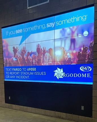 A digital display in a hallway in Fargodome advertising the stadium’s keyword for reporting issues and incidents.