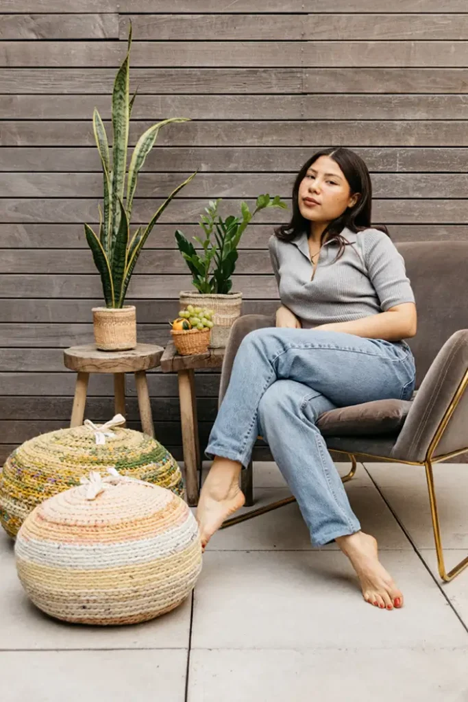 Founder Oriana sits on a chair next to plants and hand-crafted cushions from Sao New York